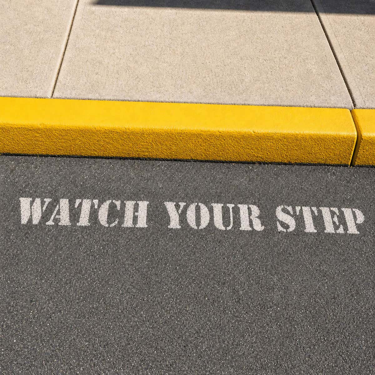 Watch Your Step stenciled onto a sidewalk next to a step