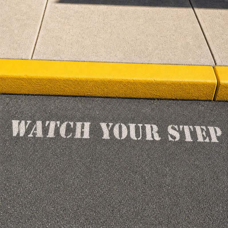 Watch Your Step stenciled onto a sidewalk next to a step