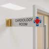 2” x 10” Corridor sign with silver material color, black engraved text, logo, and gold holder on a hallway wall with custom text saying “CARDIOLOGY ROOM”.
