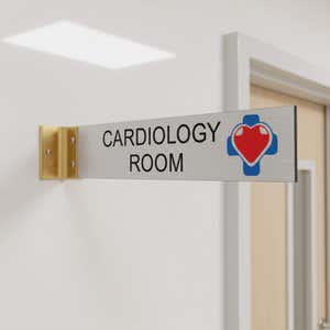 2” x 10” Corridor sign with silver material color, black engraved text, logo, and gold holder on a hallway wall with custom text saying “CARDIOLOGY ROOM”.