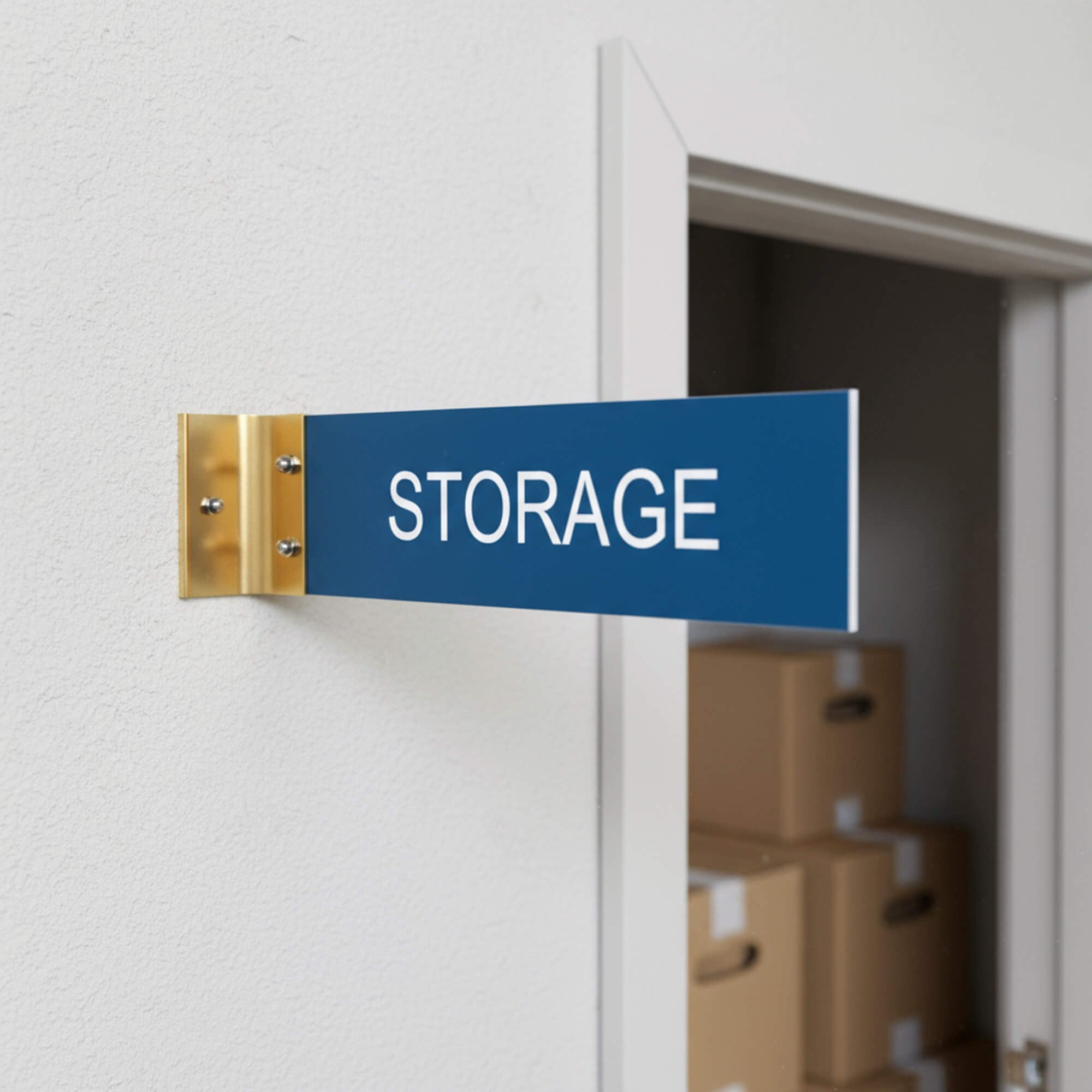 2” x 8” Corridor sign with blue material color, white engraved text, and gold holder on a hallway wall with custom text saying “STORAGE”.