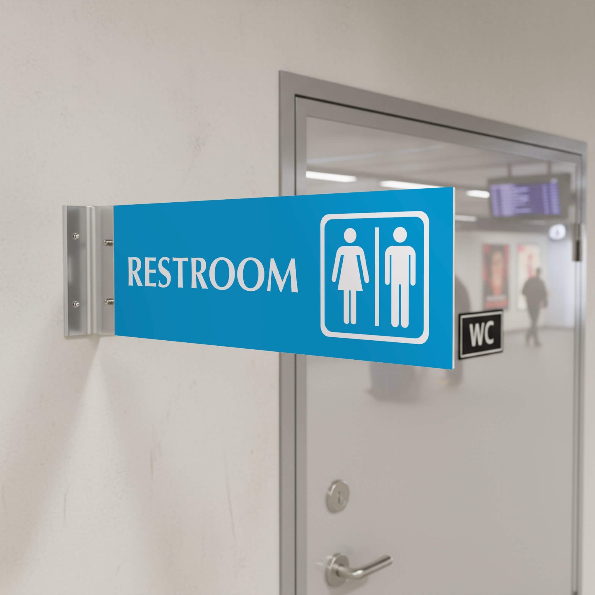 4” x 12” Corridor sign with baby blue material color, white engraved text, logo and silver holder on a hallway wall with text saying “RESTROOM”.