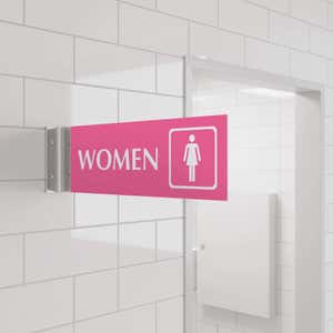 4” x 12” Corridor sign with pink material color, white engraved text, logo and silver holder on a hallway wall with text saying “WOMEN”.