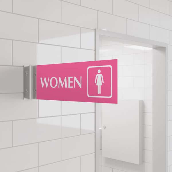 4” x 12” Corridor sign with pink material color, white engraved text, logo and silver holder on a hallway wall with text saying “WOMEN”.