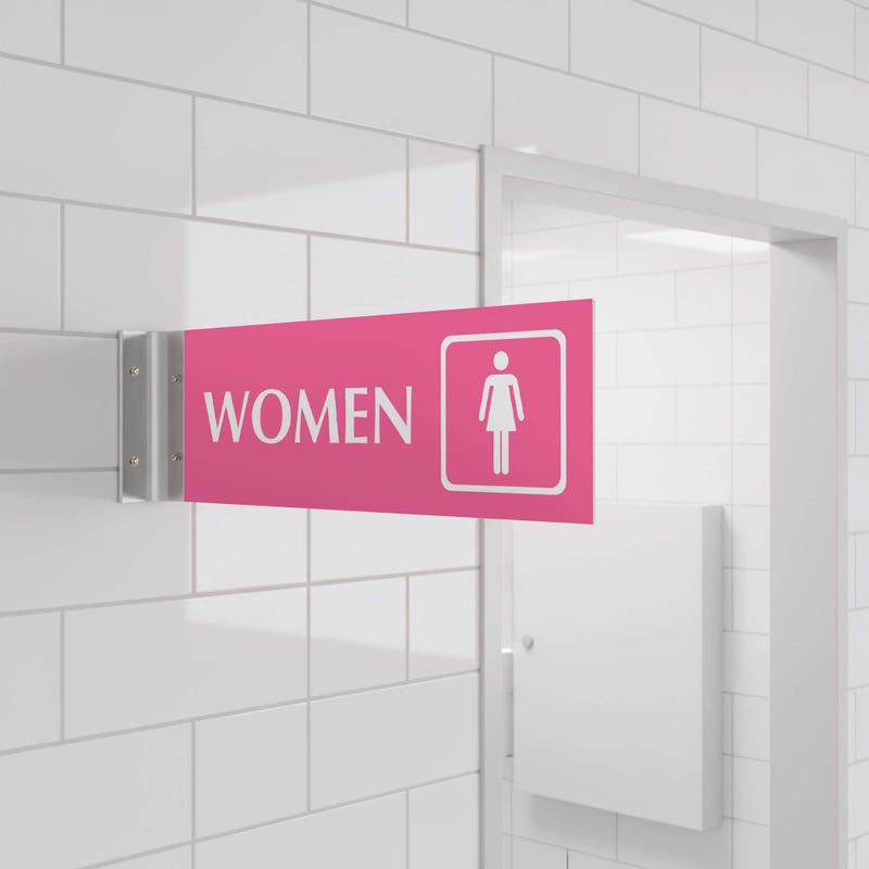 4” x 12” Corridor sign with pink material color, white engraved text, logo and silver holder on a hallway wall with text saying “WOMEN”.