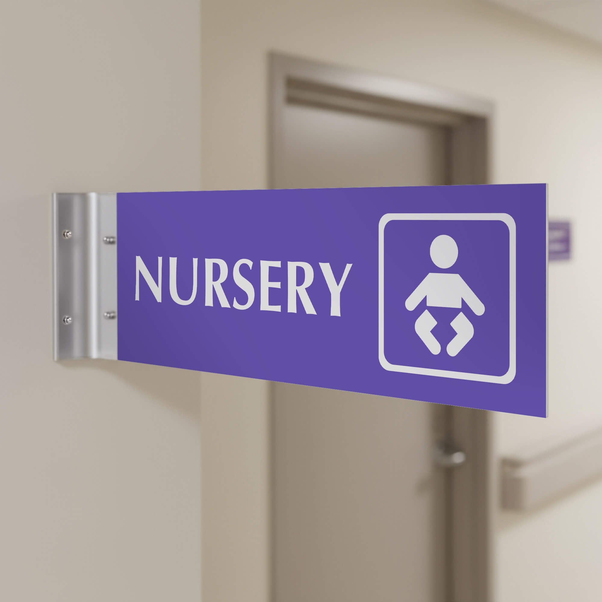 4” x 12” Corridor sign with purple material color, white engraved text, logo and silver holder on a hallway wall with text saying “NURSERY”.