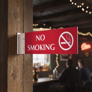 4” x 12” Corridor sign with red material color, white engraved text, logo and silver holder on a hallway wall with text saying “NO SMOKING”.