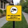 No soliciting sign with a yellow background reading Security cameras in bold hung on a pole 