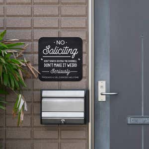 Chalkboard No soliciting design with a black background hung up outside next to the front door.