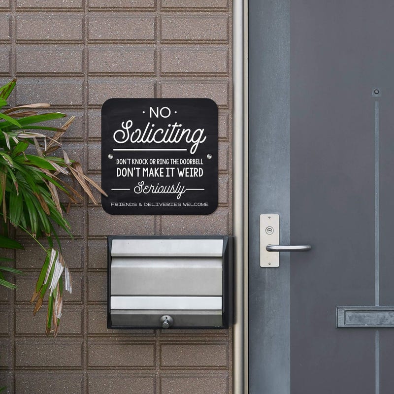 Chalkboard No soliciting design with a black background hung up outside next to the front door.