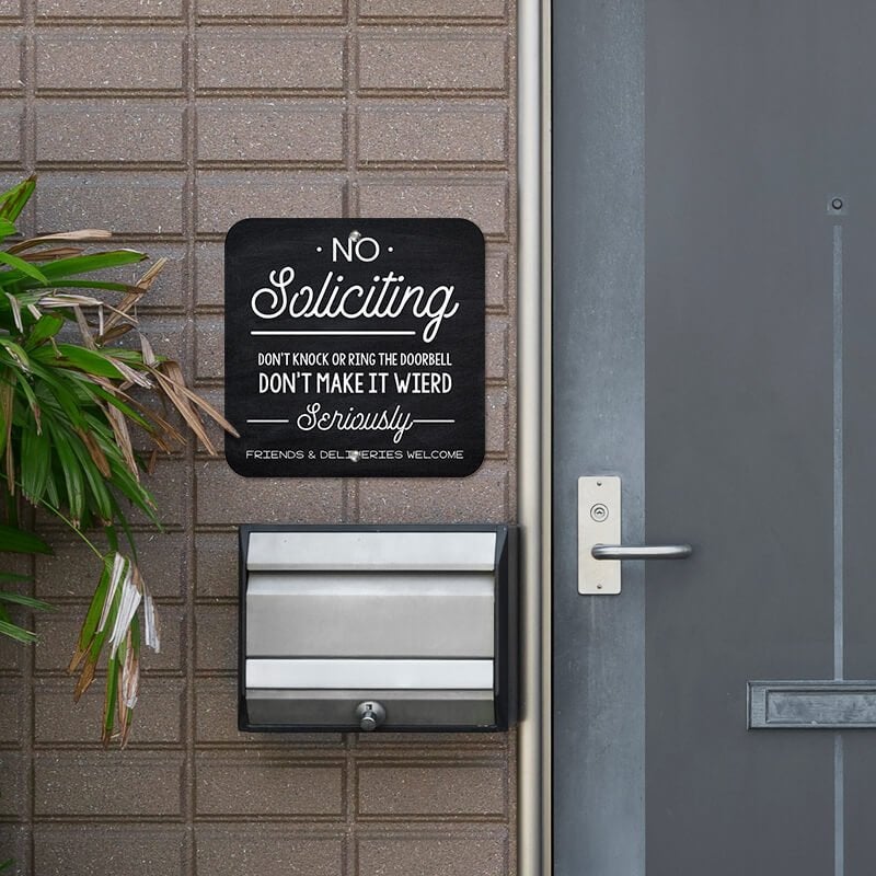 Chalkboard No soliciting design with a black background hung up outside next to the front door.