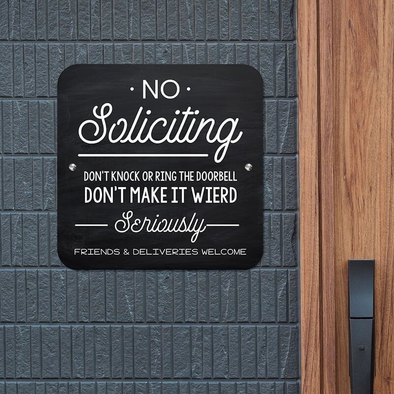 Funny black No Soliciting sign hung on the wall with white letters reading, "Don’t knock or ring the doorbell
