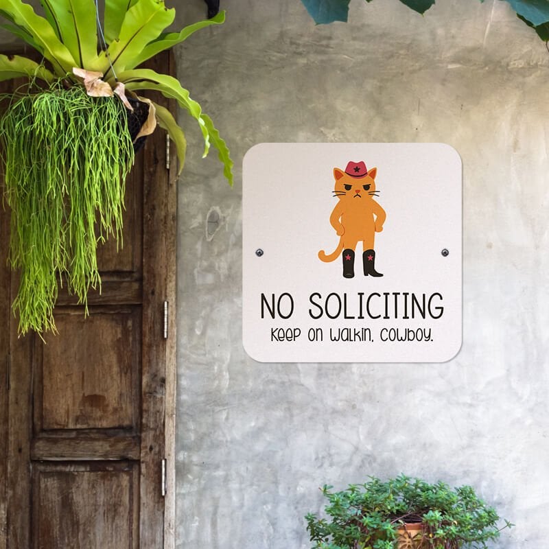 No soliciting cute cat sign reading “keep on walkin cowboy” hung up on the wall