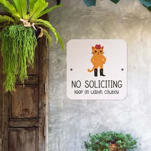 No soliciting cute cat sign reading “keep on walkin cowboy” hung up on the wall
