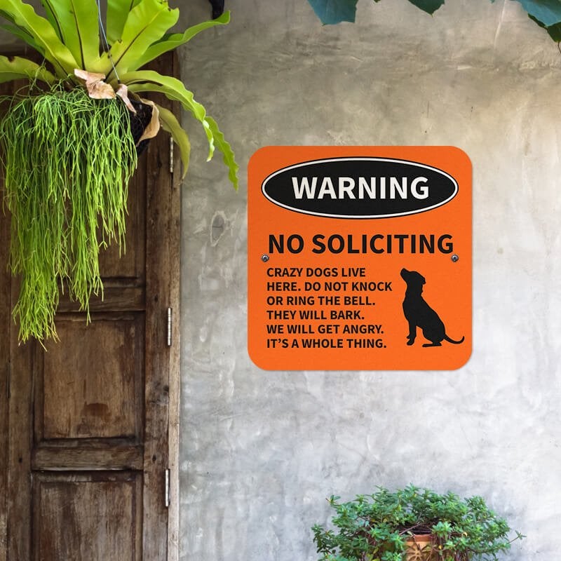 Orange no soliciting dog warning sign with a dog icon and bold text hung up on a wall