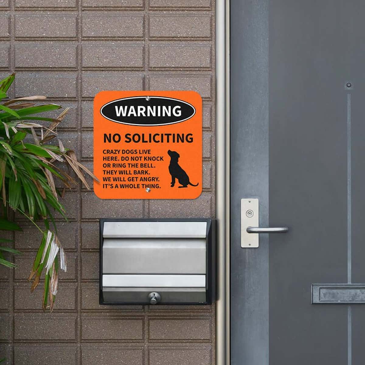 Orange no soliciting dog warning sign with a dog icon and bold text hung outside next to the front door
