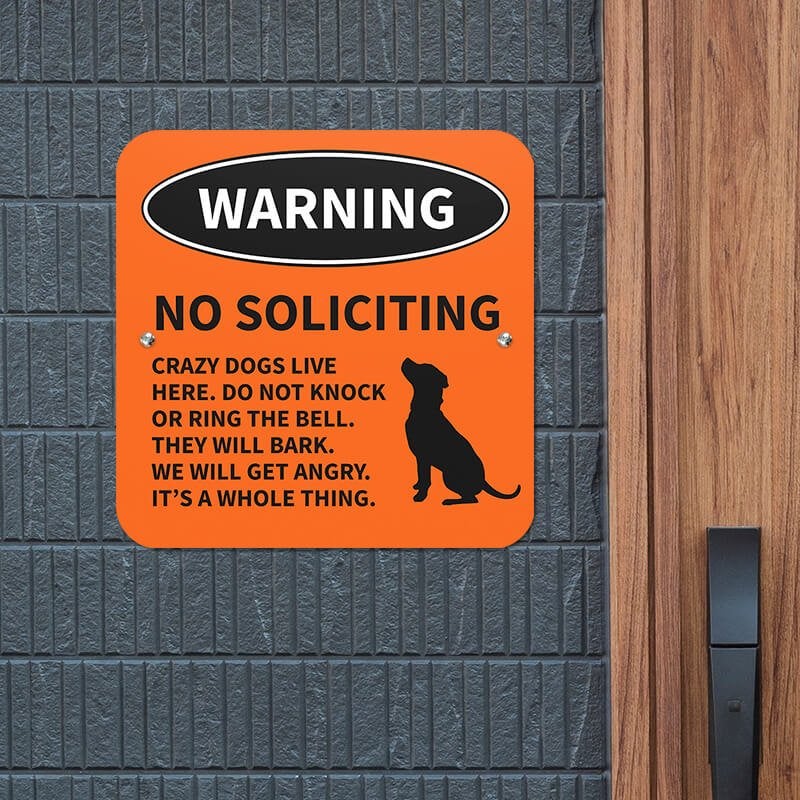 No soliciting dog warning sign with dog icon with bold text reading: “Crazy dogs live here” hung up on a gray wall