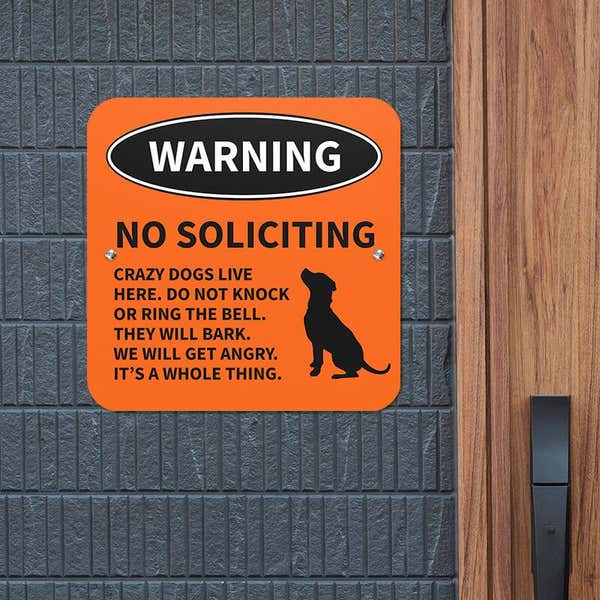 No soliciting dog warning sign with dog icon with bold text reading: “Crazy dogs live here” hung up on a gray wall