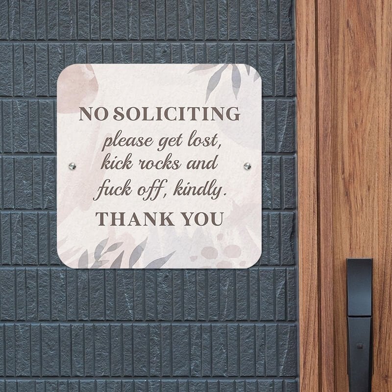 No soliciting sign on pastel floral background reading: Please get lost and kick rocks kindly, hung up on a wall.