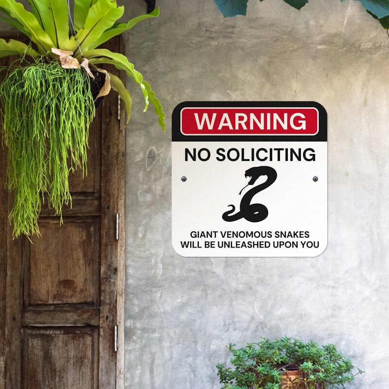 No soliciting warning sign, with snake icon, hung on a wall with giant venomous snakes will be unleashed upon you text. 
