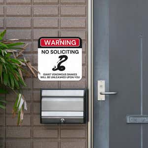 No soliciting warning sign, with a snake icon, hung next to the front door.