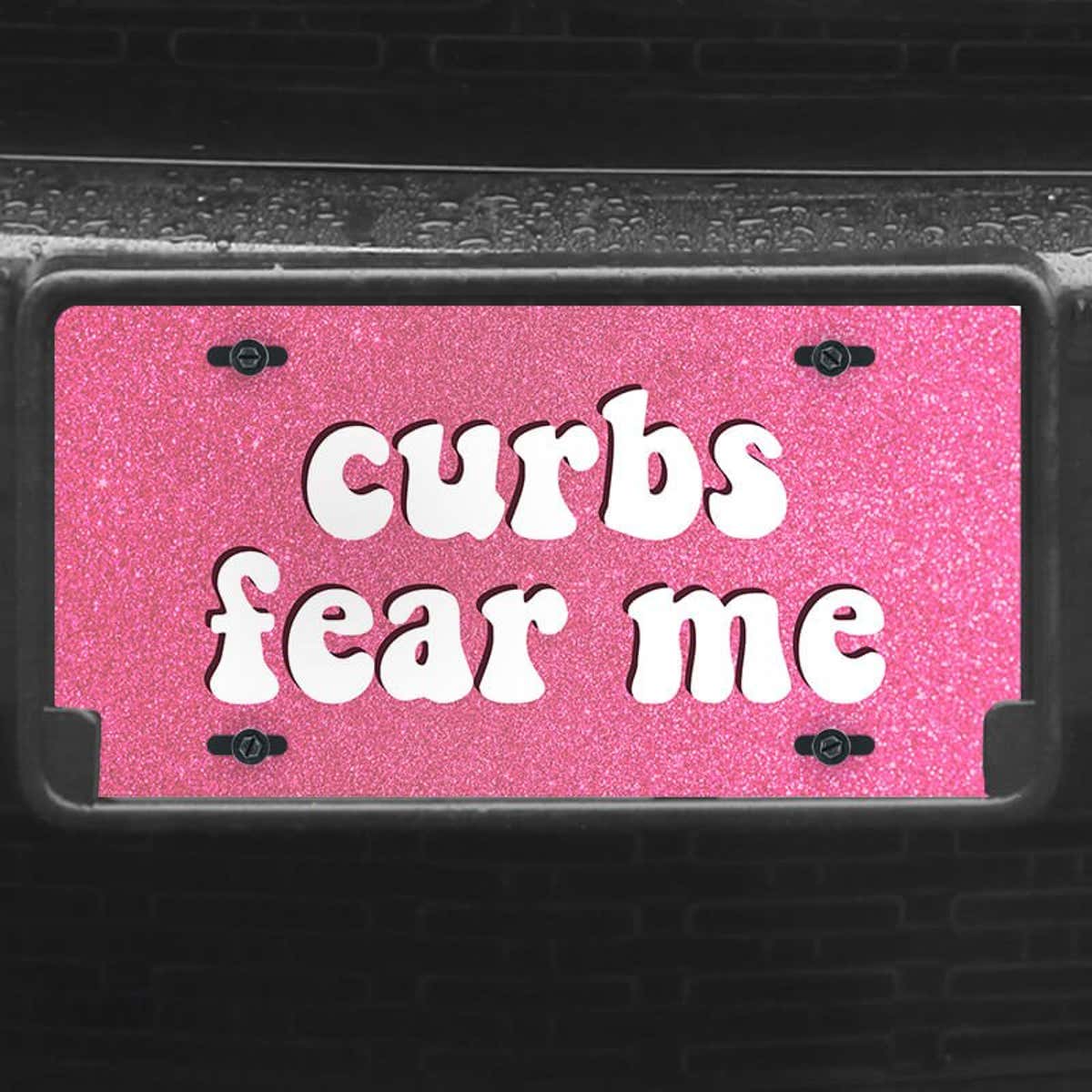 A close up of the Curbs Fear Me front license plate on a black car