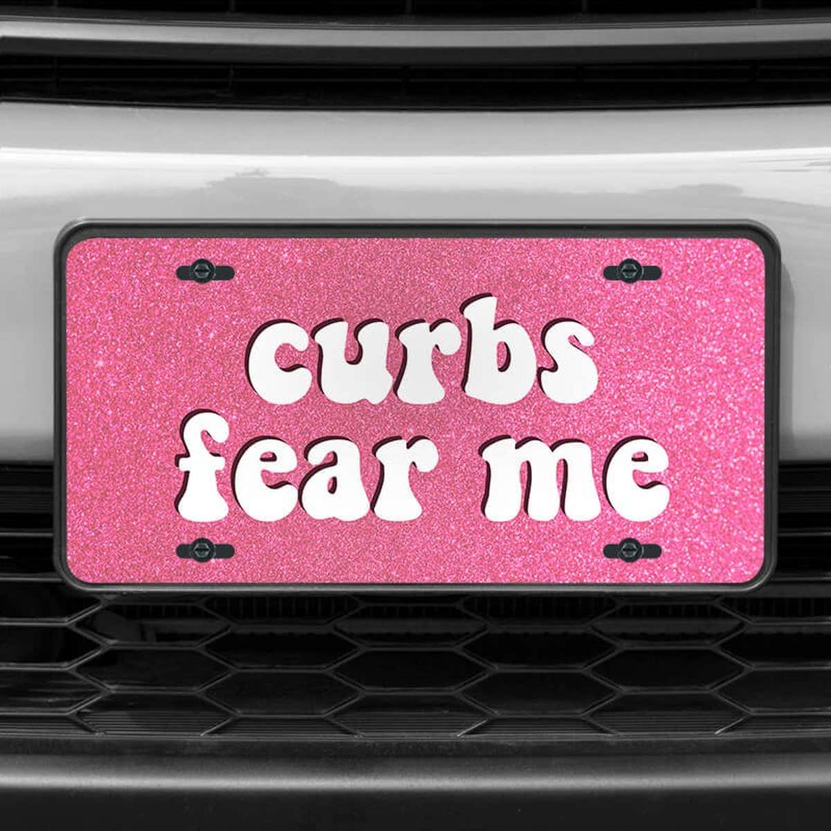 A close up of the Curbs Fear Me front license plate on a white car