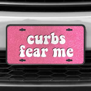 A close up of the Curbs Fear Me front license plate on a white car