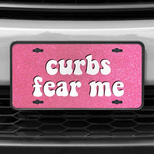 A close up of the Curbs Fear Me front license plate on a white car