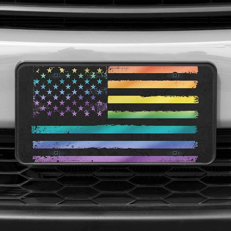 A close up of the LGBTQ Pride American Flag front license plate on a white car
