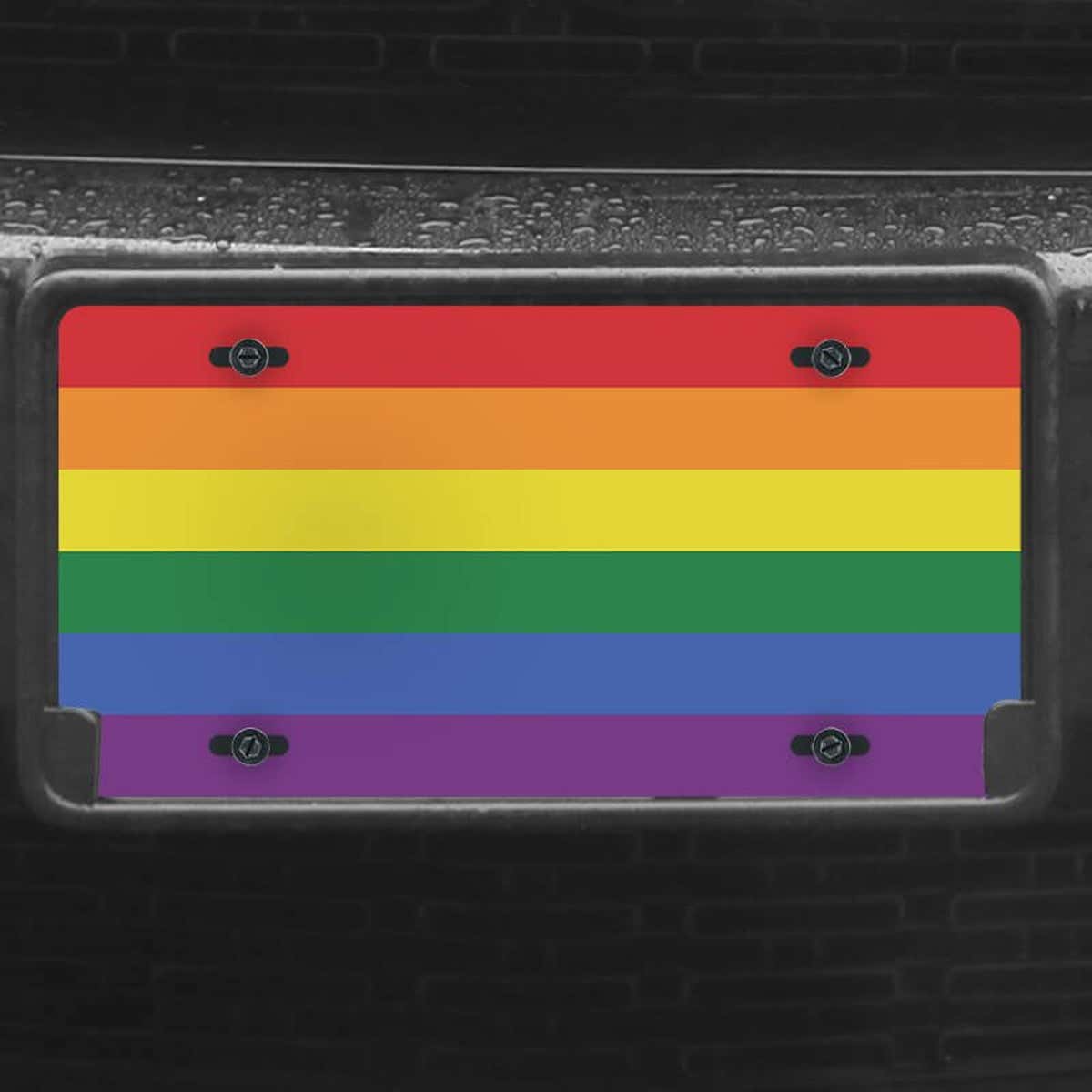A close up of the LGBTQ Pride front license plate on a black car
