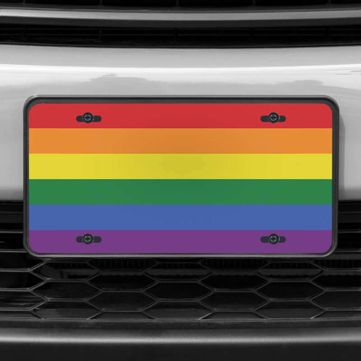A close up of the LGBTQ Pride front license plate on a white car