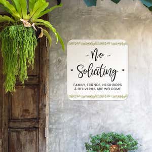 No soliciting sign, with a floral design on a white background, hung up on a wall saying family and friends are welcome
