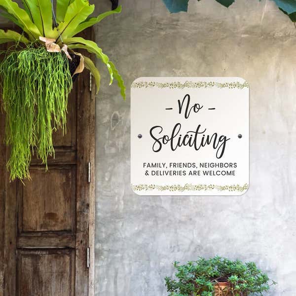 No soliciting sign, with a floral design on a white background, hung up on a wall saying family and friends are welcome