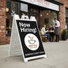 A now hiring sidewalk sign in front of a cafe