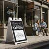 A We Are Open sandwich board sign displayed in front of a coffee shop with their logo on the sign