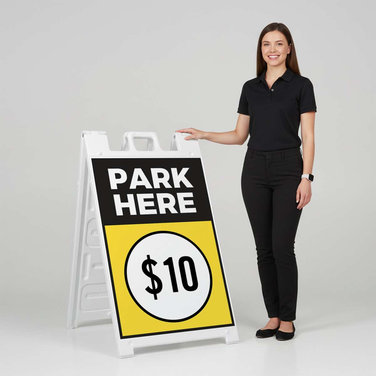 A woman standing next to the park here A-frame sign with her hand on the top of the sign