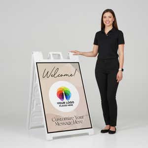 A woman standing next to a Welcome A-frame sign with her hand on the top of the sign