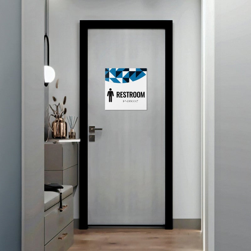 A 2-layered ADA sign for a restroom with a white foreground and a blue geometric background