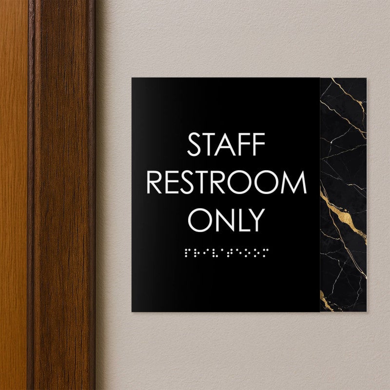 A modern layered ADA sign for a staff restroom hung next to a doorway