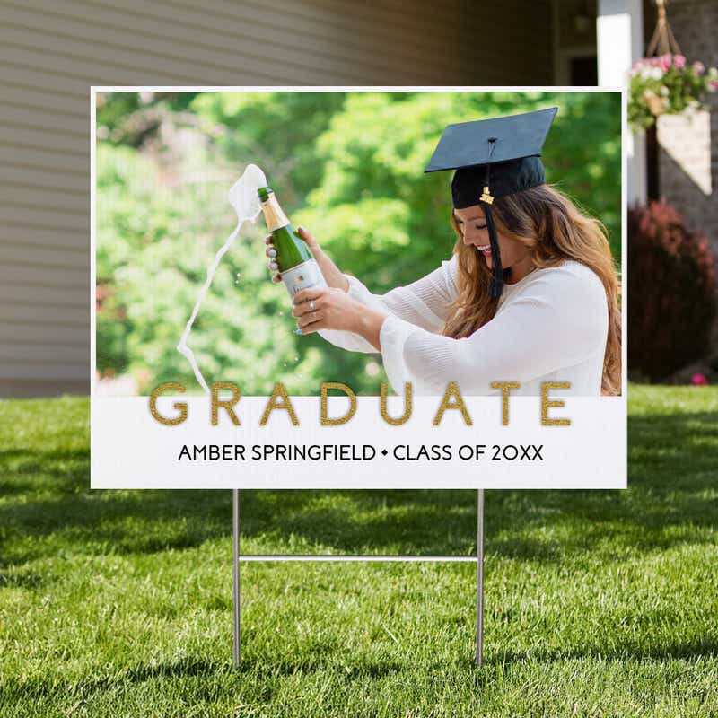Gold text graduation yard sign displayed in a front yard