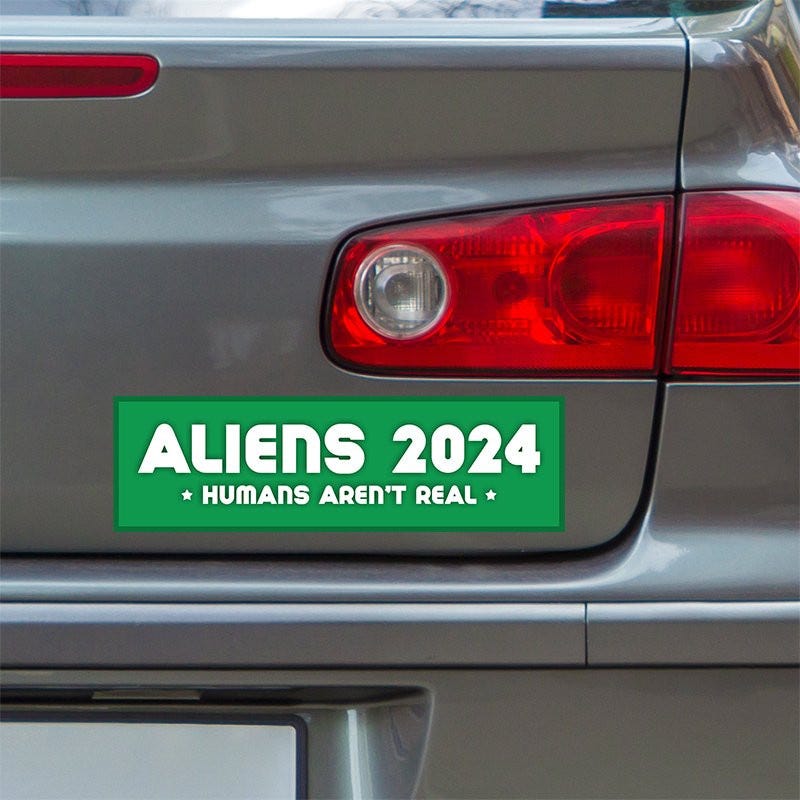 Aliens - Humans Aren't Real Bumper Sticker below a gray car's tail light