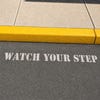 Watch Your Step sprayed onto a sidewalk using a stencil