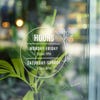 Round business hours decal on a window with greenery behind it