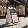 A sidewalk sign displayed outside of a boutique that says We Are Open and features their logo