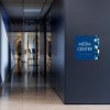 A large layered ADA sign for a media center with a blue foreground and blue geometric background