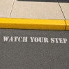 Watch Your Step sprayed onto a sidewalk using a stencil