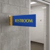 4” x 12” Corridor sign with blue material color, yellow engraved text, and gold holder on a hallway wall with text saying “RESTROOM”.