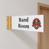 4” x 12” Corridor sign with white material color, black engraved text, logo, and gold holder on a hallway wall with custom text saying “BAND ROOM”.