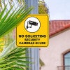 No soliciting sign with a yellow background reading Security cameras in bold hung on a pole 